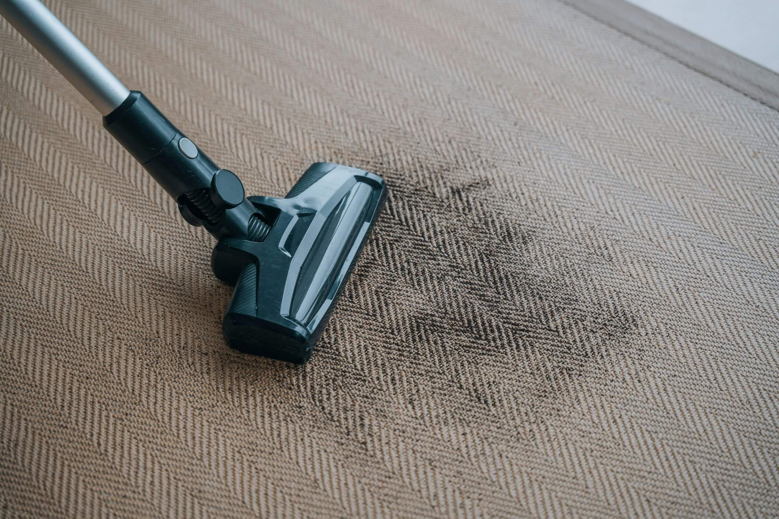 A vacuum cleaner is being used to clean a patterned rug with a visible patch of dirt or stains, highlighting the importance of regular carpet care for a fresher, cleaner home.