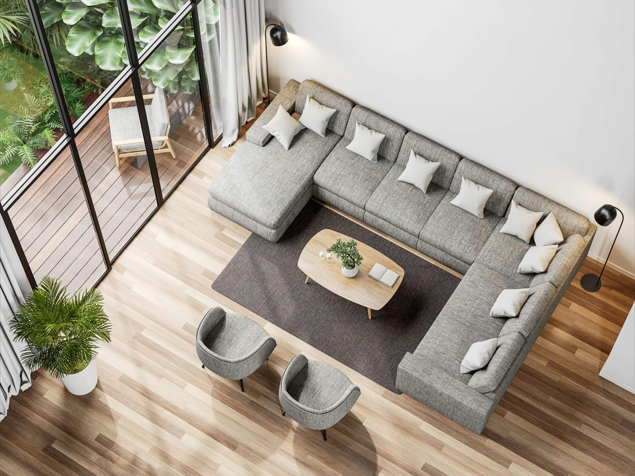 A modern living room with a large gray sectional sofa, two gray chairs, a wooden coffee table, and a dark rug showcases the latest flooring trends with stylish wood flooring. Floor-to-ceiling windows overlook a green patio with plants.